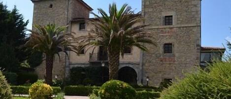 A stone building with a central courtyard, palm trees, and a paved walkway.