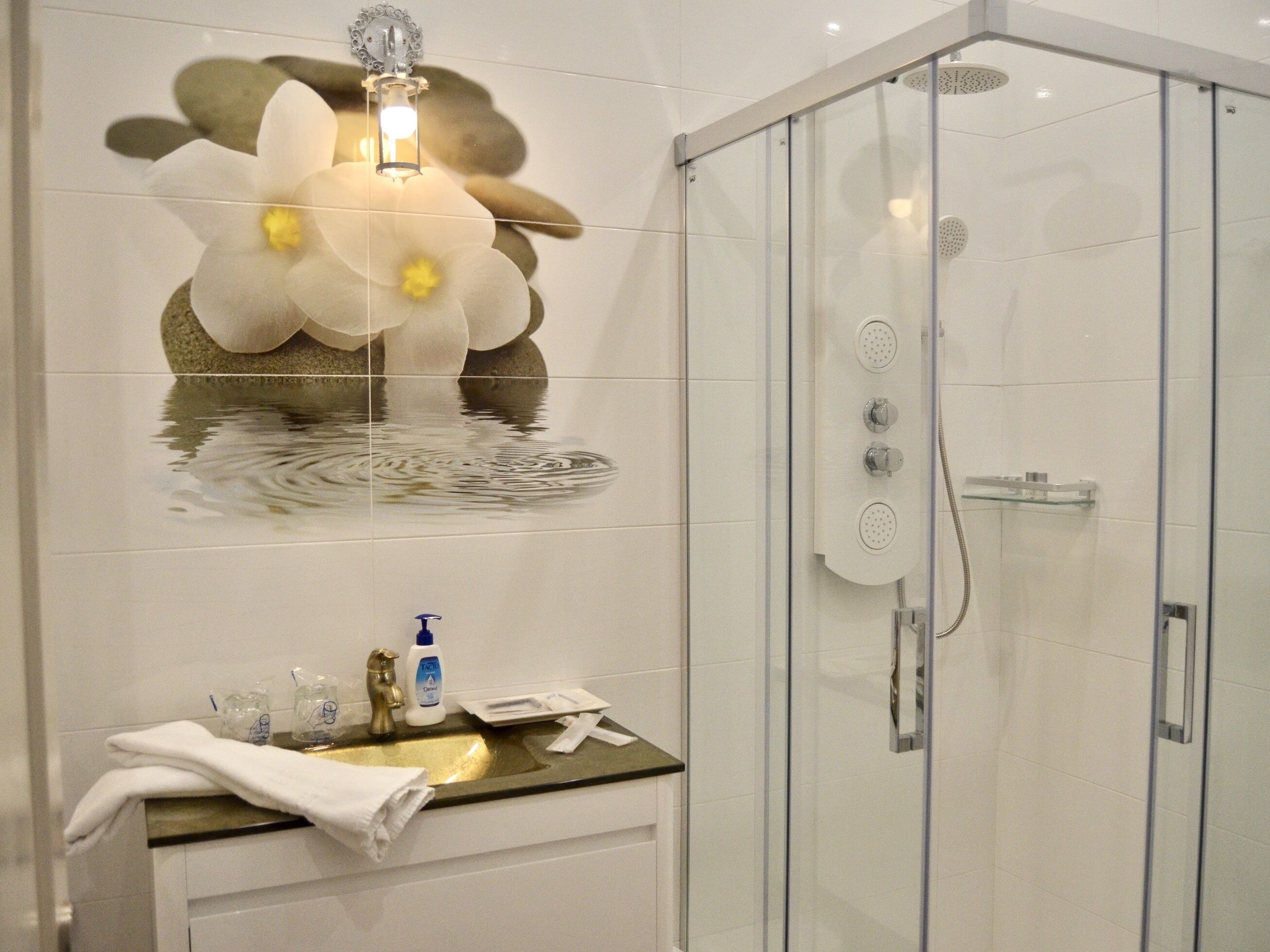 A modern bathroom with a glass shower enclosure, a sink with a gold faucet, and a decorative wall with a flower design.