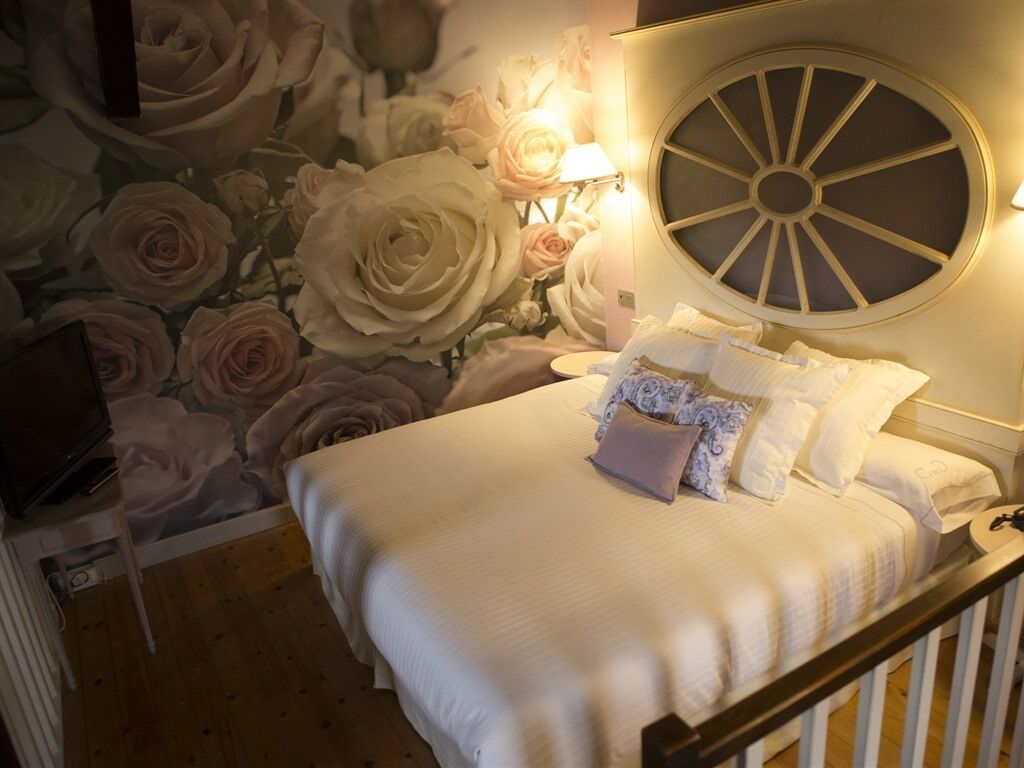 A bedroom with a large floral wallpaper, a round wall clock, and a bed with white bedding and multiple pillows.