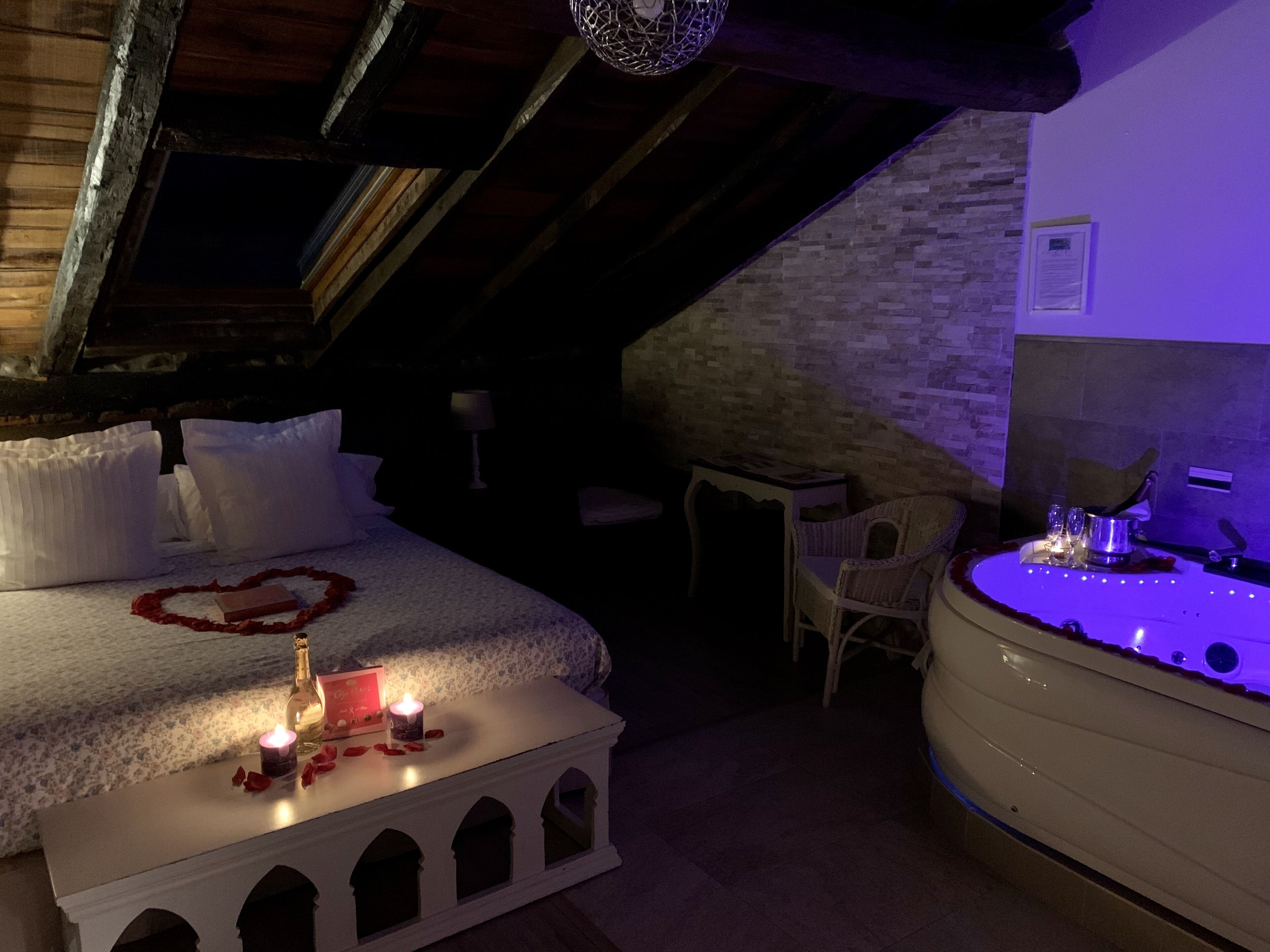 A cozy attic bedroom with a bed, bedside table, and a bathtub with lights.