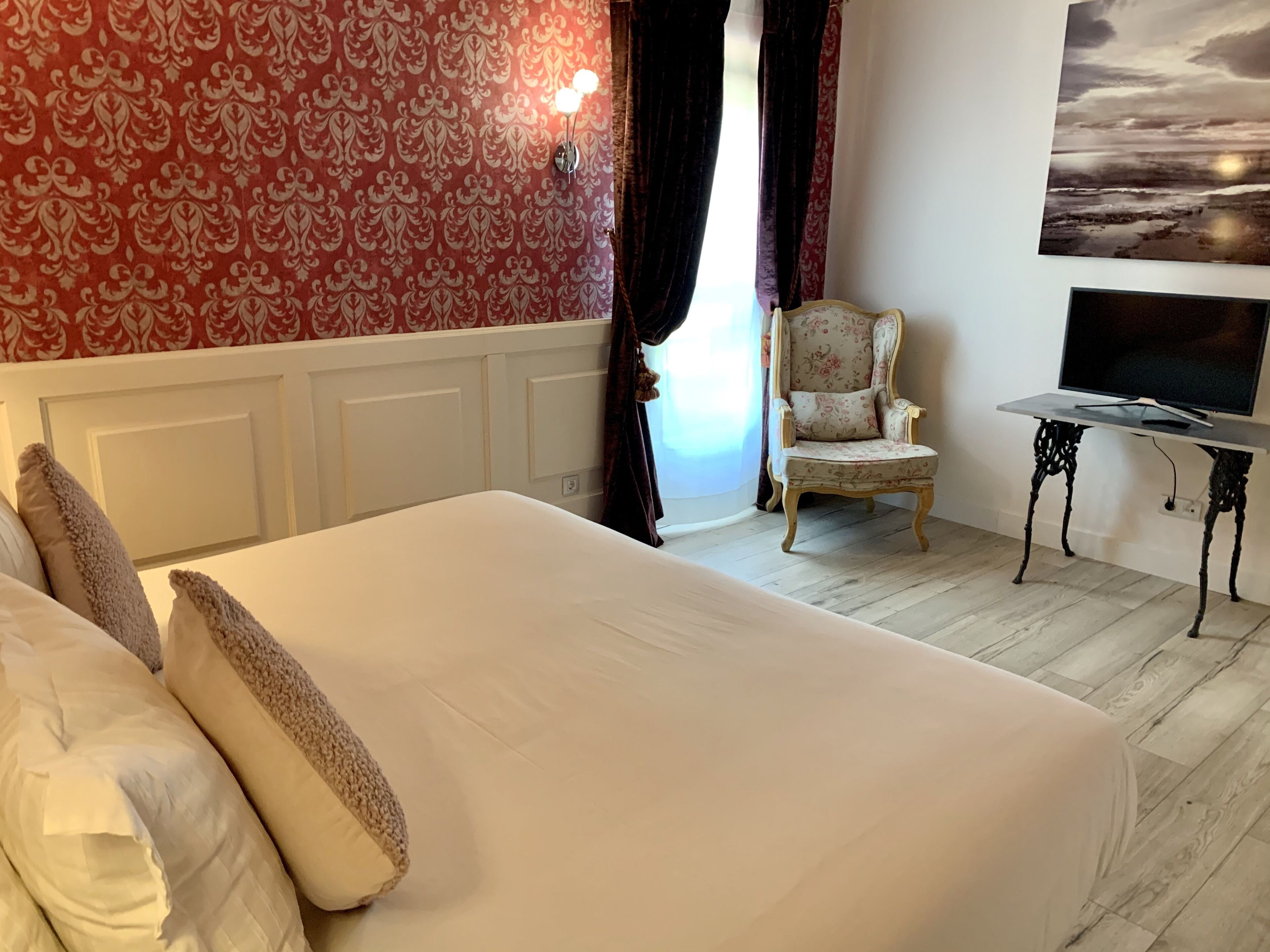 Een slaapkamer met een groot bed, een stoel, een klein tafeltje en een televisie.