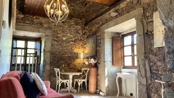 Un interior rústico con paredes de piedra vista, una araña, un sofá rojo y una zona de comedor.