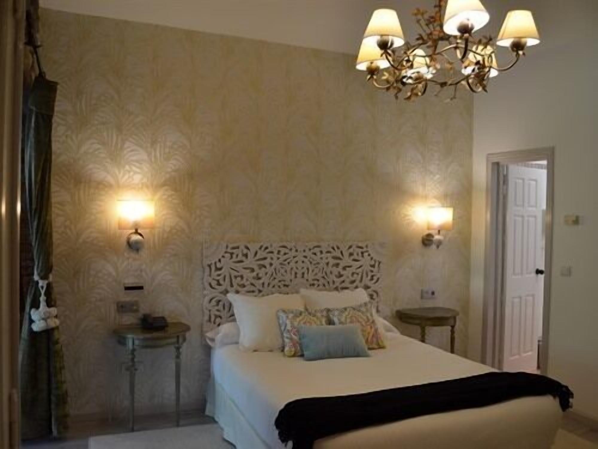 A bedroom with a bed, two bedside tables, a chandelier, and wall sconces.