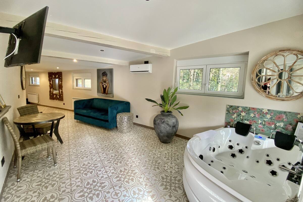 A modern bathroom with a large bathtub, a small table with chairs, a sofa, and a decorative mirror.
