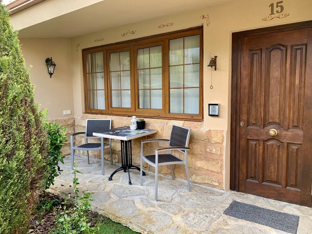 Un patio de piedra con una mesa y dos sillas, una puerta de madera y un ventanal con vidrio satinado.