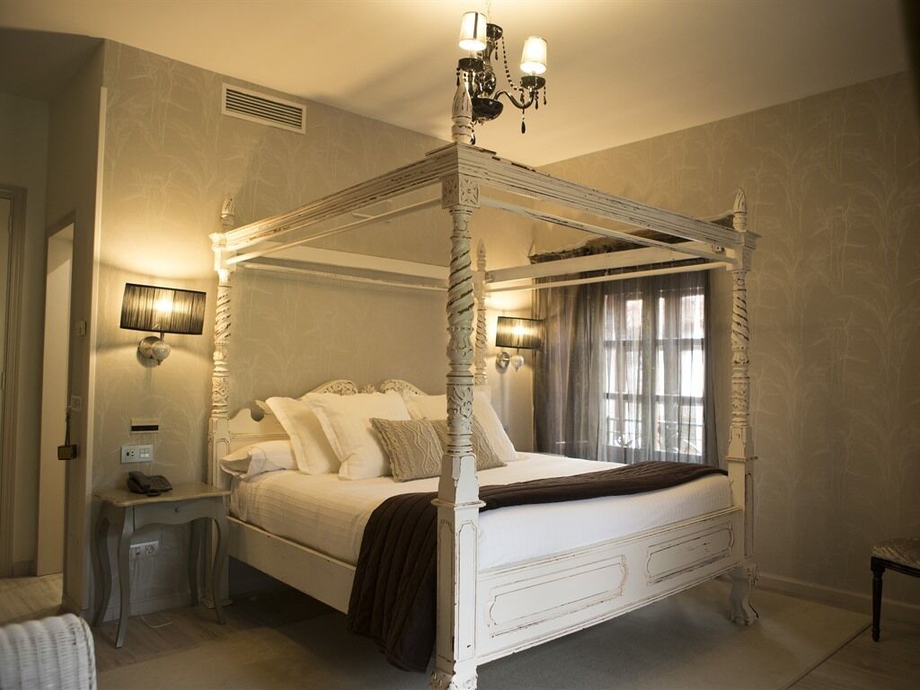 A four-poster bed with a canopy, bedside lamps, and a nightstand with a telephone.