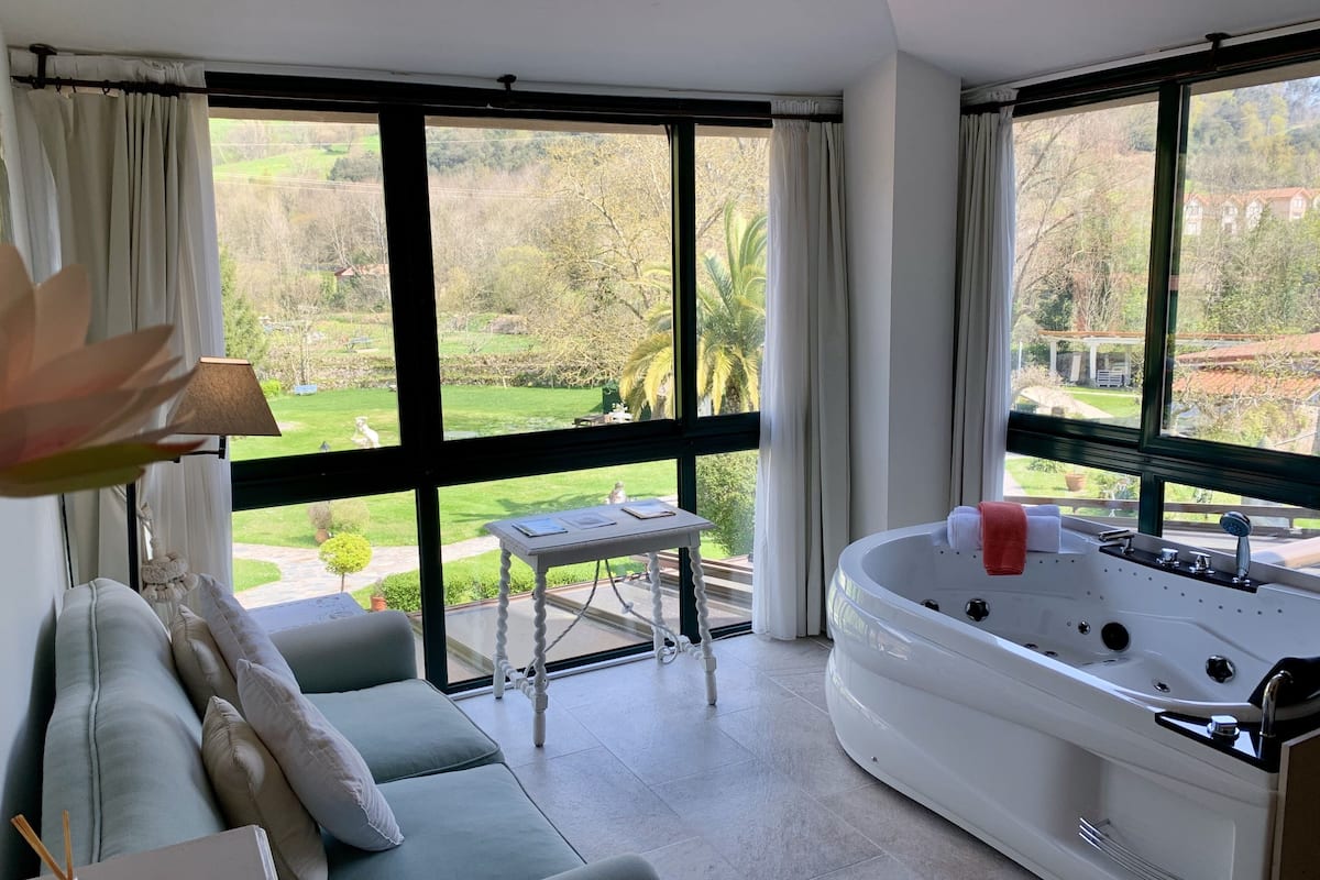 A room with a large window, a sofa, a small table, and a hot tub.