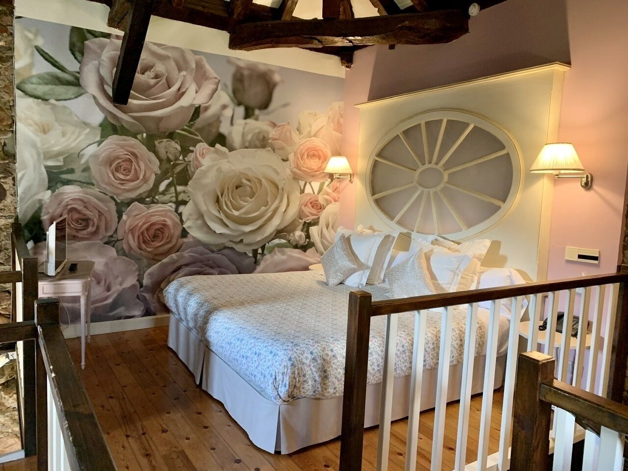 Un dormitorio con un amplio mural floral, un ventanal redondo y dos lámparas fijadas a la pared.