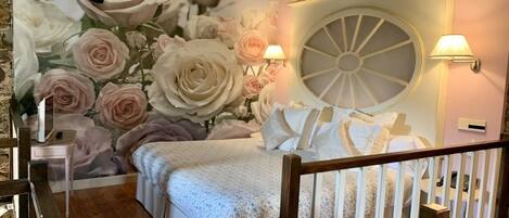 Un dormitorio con un amplio mural floral, un ventanal redondo y dos lámparas fijadas a la pared.