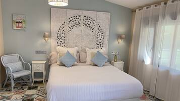 A bedroom with a large bed, a chair, a bedside table, a wall-mounted lamp, and a decorative panel above the bed.
