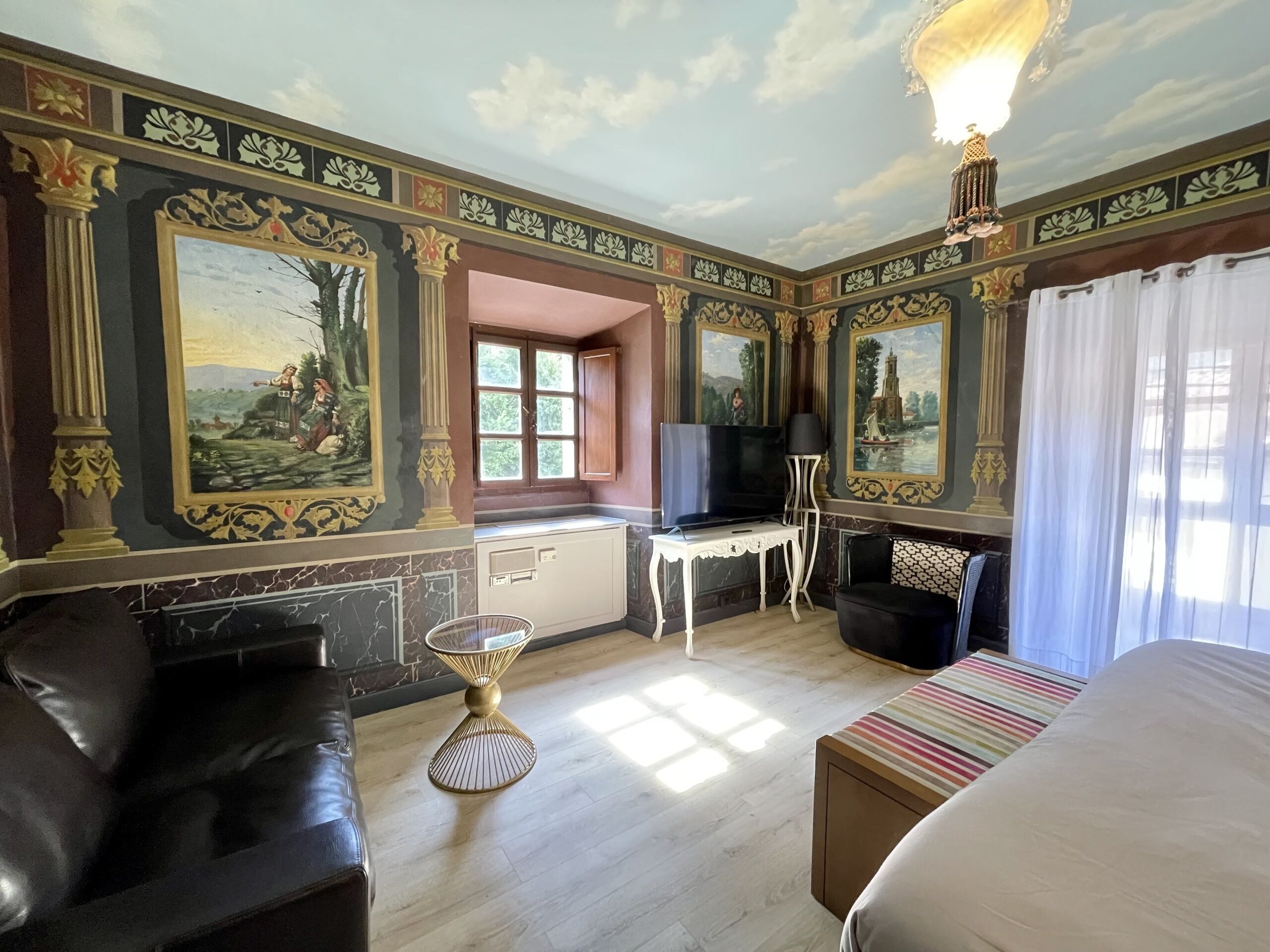 Una habitación con una cama grande, un sofá de cuero negro, una mesita y un televisor.
