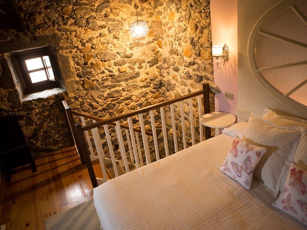 A bedroom with a stone wall, a wooden bed, a nightstand, and a small window.