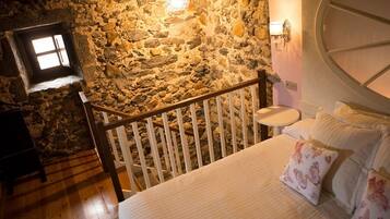 Un dormitorio con pared de piedra, cama de madera, mesita de noche y una ventana pequeña.