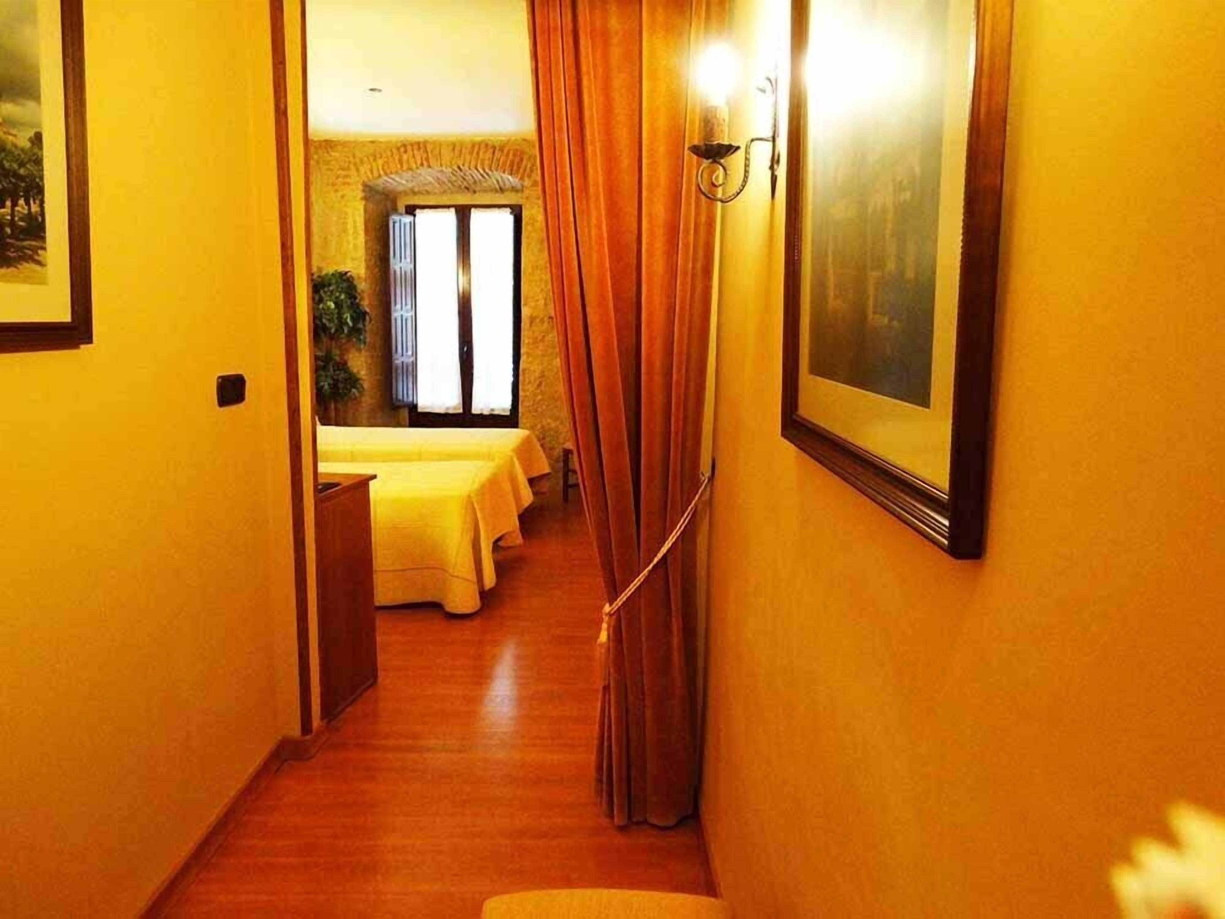 Un pasillo estrecho con suelo de madera que conduce a una habitación con dos camas cubiertas de sábanas amarillas.