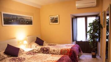 Habitación de hotel con dos camas, una mesita de noche, una lámpara, una planta en maceta y una ventana con cortinas.
