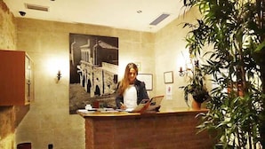 A reception desk with a person seated, a large framed picture on the wall, and a potted plant to the right. - Palacio Antigua Audiencia (Ciudad Rodrigo)