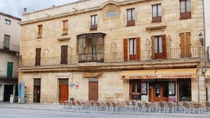A two-story building with a cafe named "CAFETERIA ARCOS PLATOS COMBINADOS" on the ground floor. There are outdoor seating areas with chairs and tables. - Palacio Antigua Audiencia (Ciudad Rodrigo)