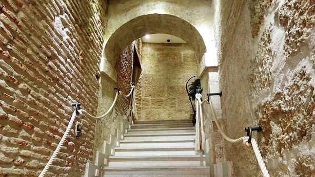 A staircase with a brick wall on one side and a white wall on the other, leading to an arched doorway. - Palacio Antigua Audiencia (Ciudad Rodrigo)