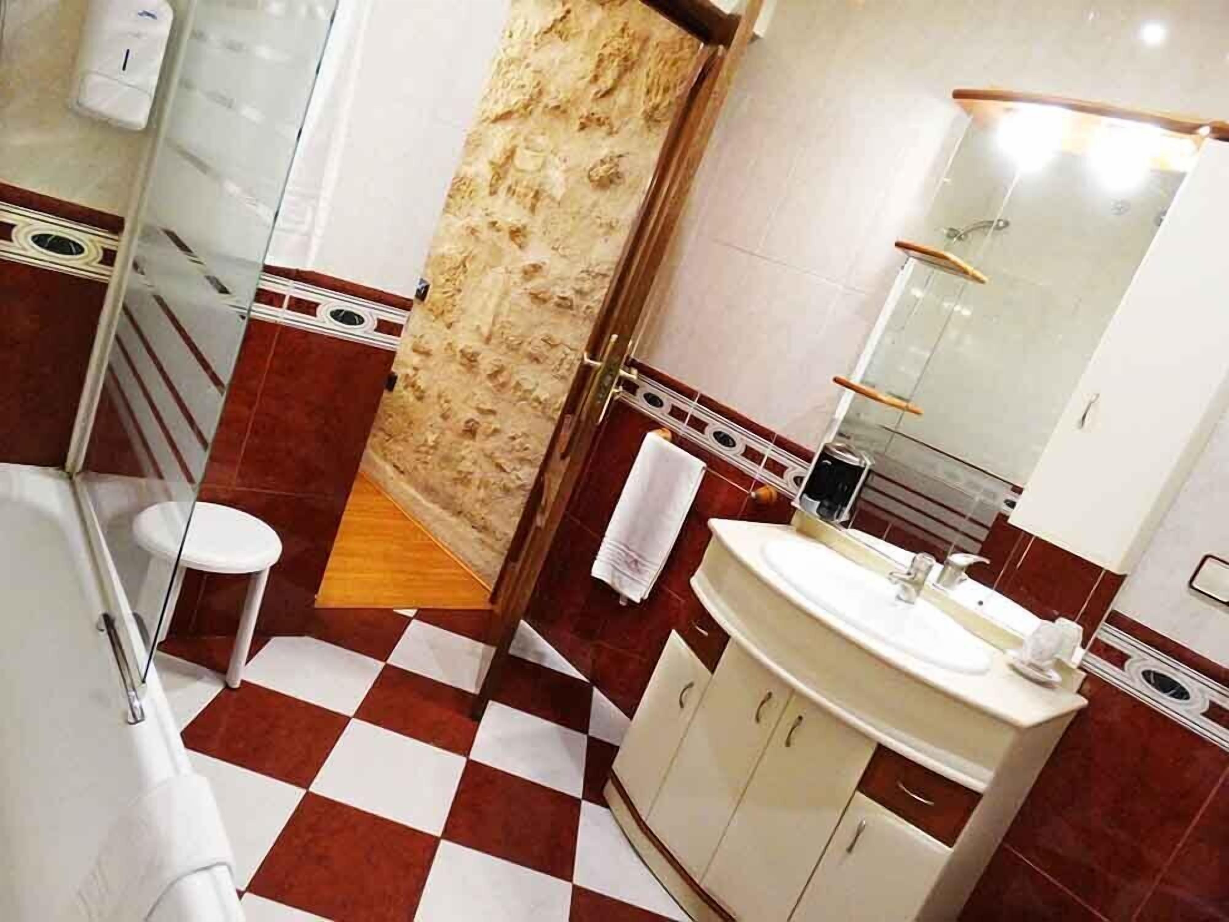 Uma casa de banho com chão xadrez, pia, espelho e zona de duche.