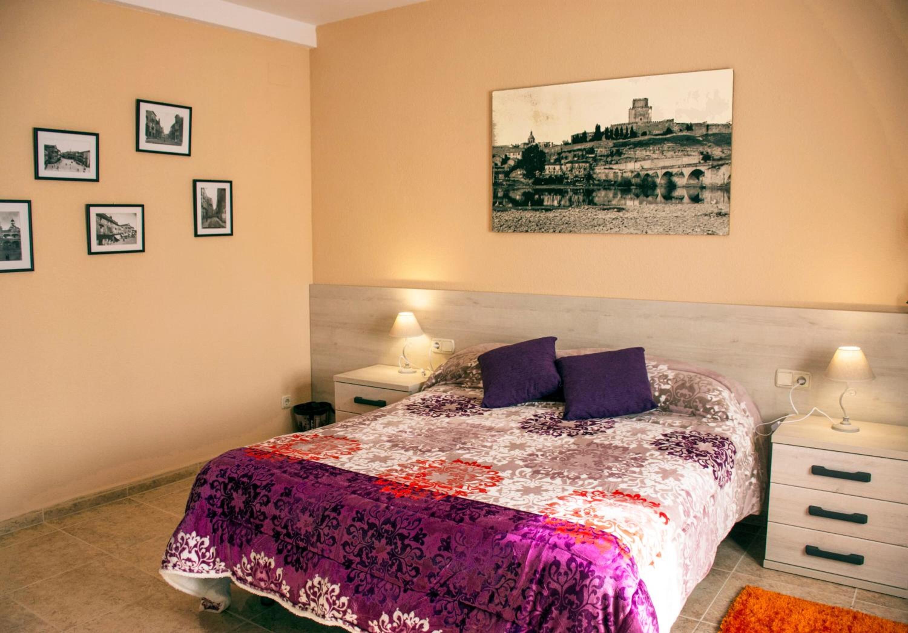 A bedroom with a bed, two bedside tables, a nightstand, a wall-mounted picture, and a floor lamp.