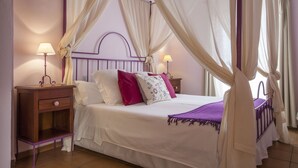 Un dormitorio con cama con dosel, dos mesitas de noche con lámparas y una manta morada.
