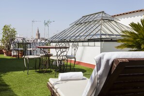 Un jardín en la azotea con un invernadero de vidrio, mobiliario para exterior y vistas a un paisaje urbano.