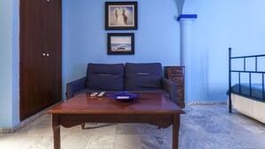 Una habitación con una mesa de madera, dos sofás azules, un armario de madera oscura y una cama con estructura metálica.