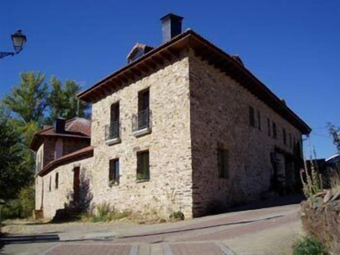 Un edificio de piedra con techo inclinado, varias ventanas y una chimenea.