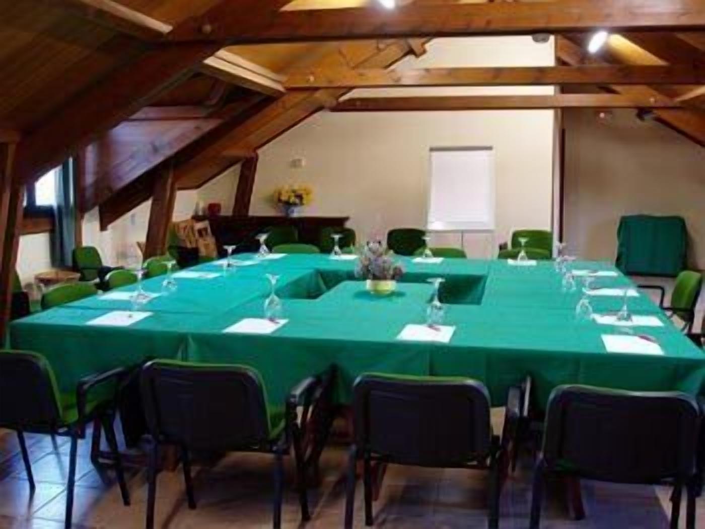 Un salón de conferencias con una larga mesa cubierta por un mantel verde, rodeada de sillas.