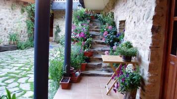 Un patio de paredes de piedra con suelo de baldosas, rodeado de plantas y flores en macetas.