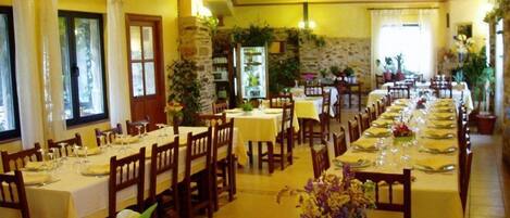 Un restaurante con varias mesas dispuestas para comer, que presenta una pared de piedra y vigas de madera.