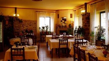 A restaurant with multiple tables and chairs, stone walls, and potted plants.