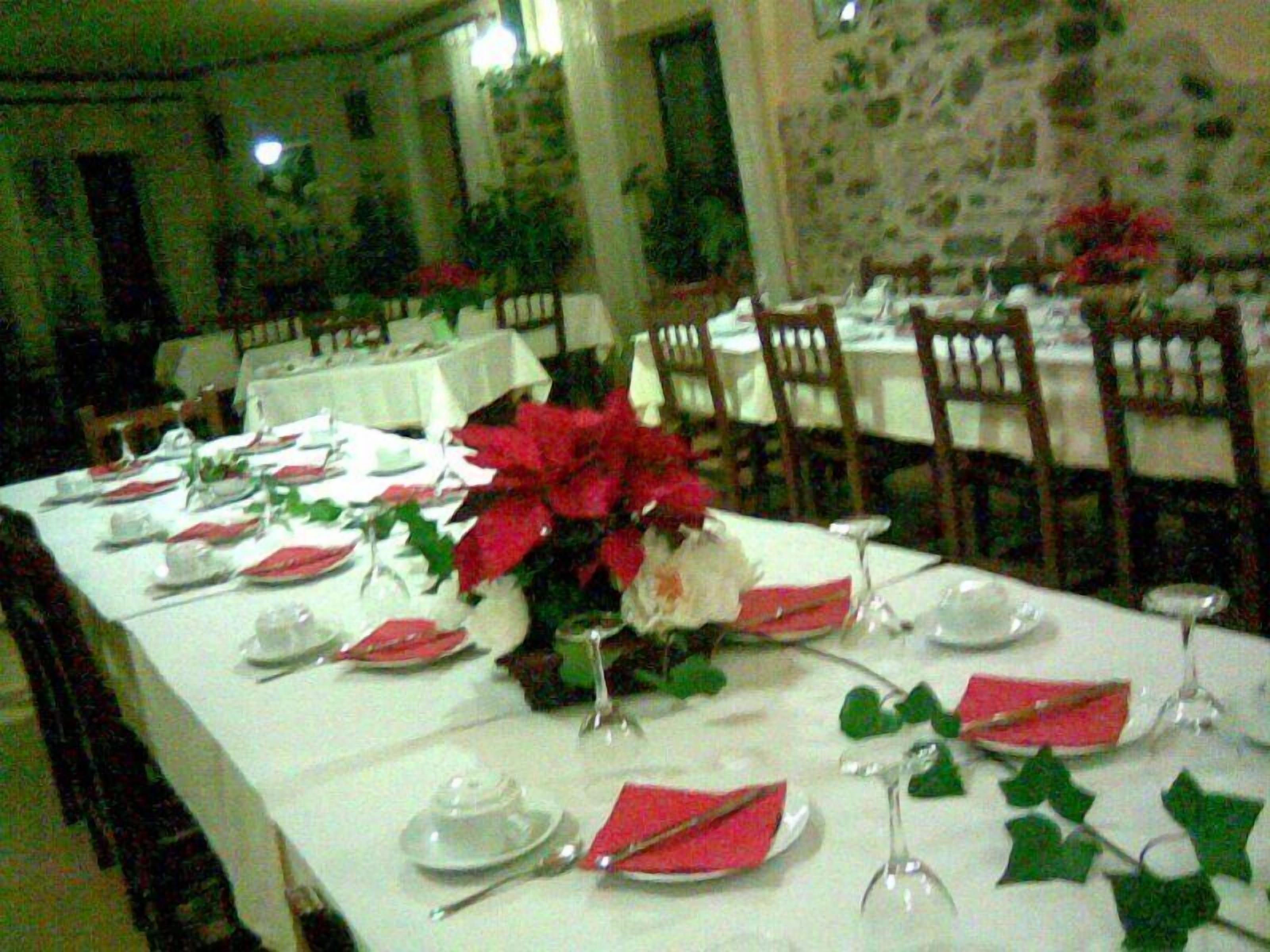 Una mesa de comedor lista para una comida, con manteles blancos, servilletas rojas y un centro de mesa de flores rojas.