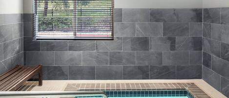 A pool area with a bench, a window with blinds, and tiled walls.