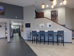 A hotel lobby with a reception desk, bar area with chairs, a staircase, and a hallway leading to other rooms. - Garner Auburn - Seattle by IHG (Auburn)