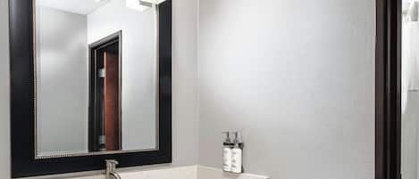 A bathroom with a large mirror, a sink, and two Dove hand sanitizer bottles on a shelf.