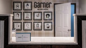 A hotel lobby with a wall of framed portraits, a reception desk, and a door to the right. - Garner Auburn - Seattle by IHG (Auburn)