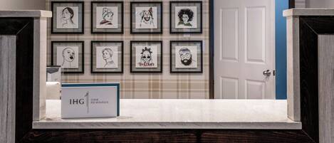 Un vestíbulo de hotel con una pared de retratos enmarcados, una recepción y una puerta a la derecha.