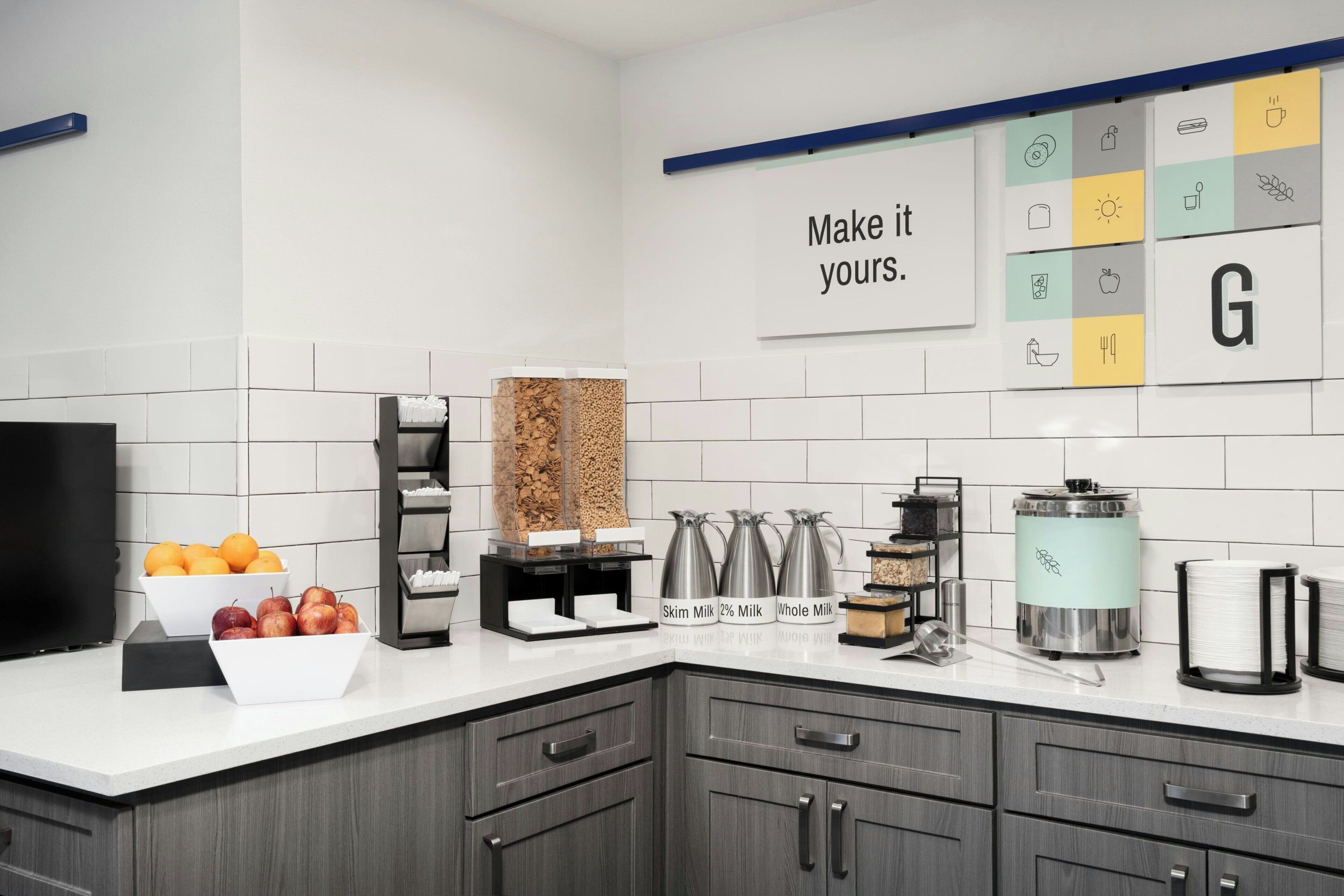 A modern kitchen with a white tiled backsplash, a black countertop, and a wall-mounted sign that reads 'Make it yours.'