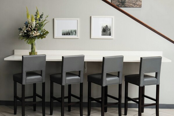 A modern kitchen with a white countertop, four black bar stools, and two framed pictures on the wall. - Garner Auburn - Seattle by IHG (Auburn)