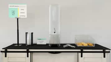 A self-service station with a water dispenser, a container for utensils, and a box of cookies.