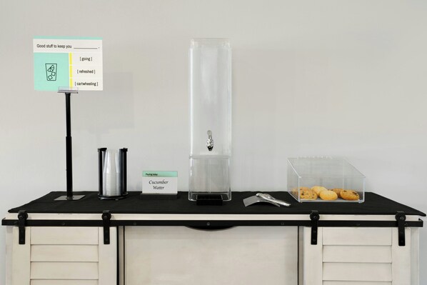 A self-service station with a water dispenser, a container for utensils, and a box of cookies. - Garner Auburn - Seattle by IHG (Auburn)