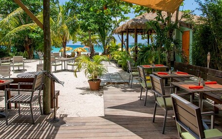 A wooden deck with tables and chairs, surrounded by palm trees and a beach view.
