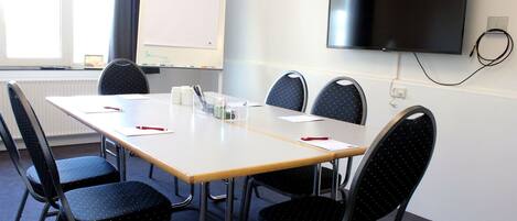 A conference room with a long table, six chairs, a whiteboard, and a TV mounted on the wall.