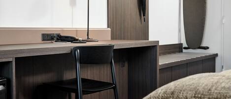 A compact workspace with a desk, chair, lamp, and ironing board.