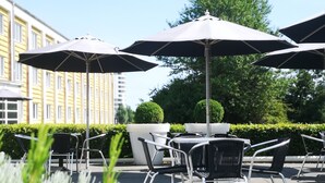 Outdoor seating with umbrellas, a potted plant, and a building in the background. - Milling Hotel Vejle (Vejle)