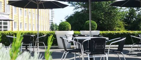 Outdoor seating with umbrellas, a potted plant, and a building in the background.