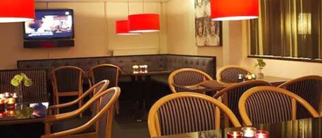 A restaurant with wooden chairs, a glass table, red pendant lights, and a television on the wall.