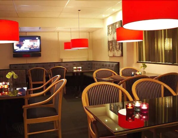A restaurant with wooden chairs, a glass table, red pendant lights, and a television on the wall. - Milling Hotel Vejle (Vejle)