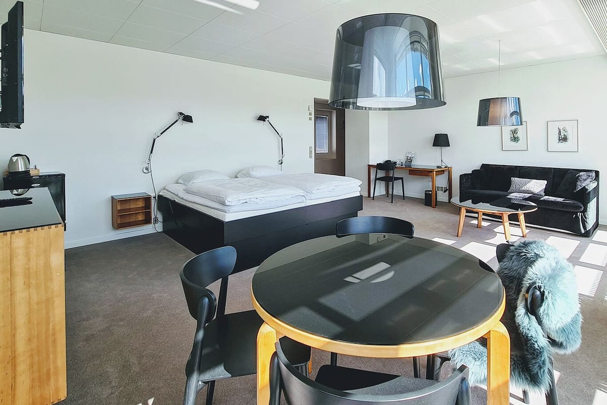 A modern hotel room with a bed, desk, chair, and a round table.